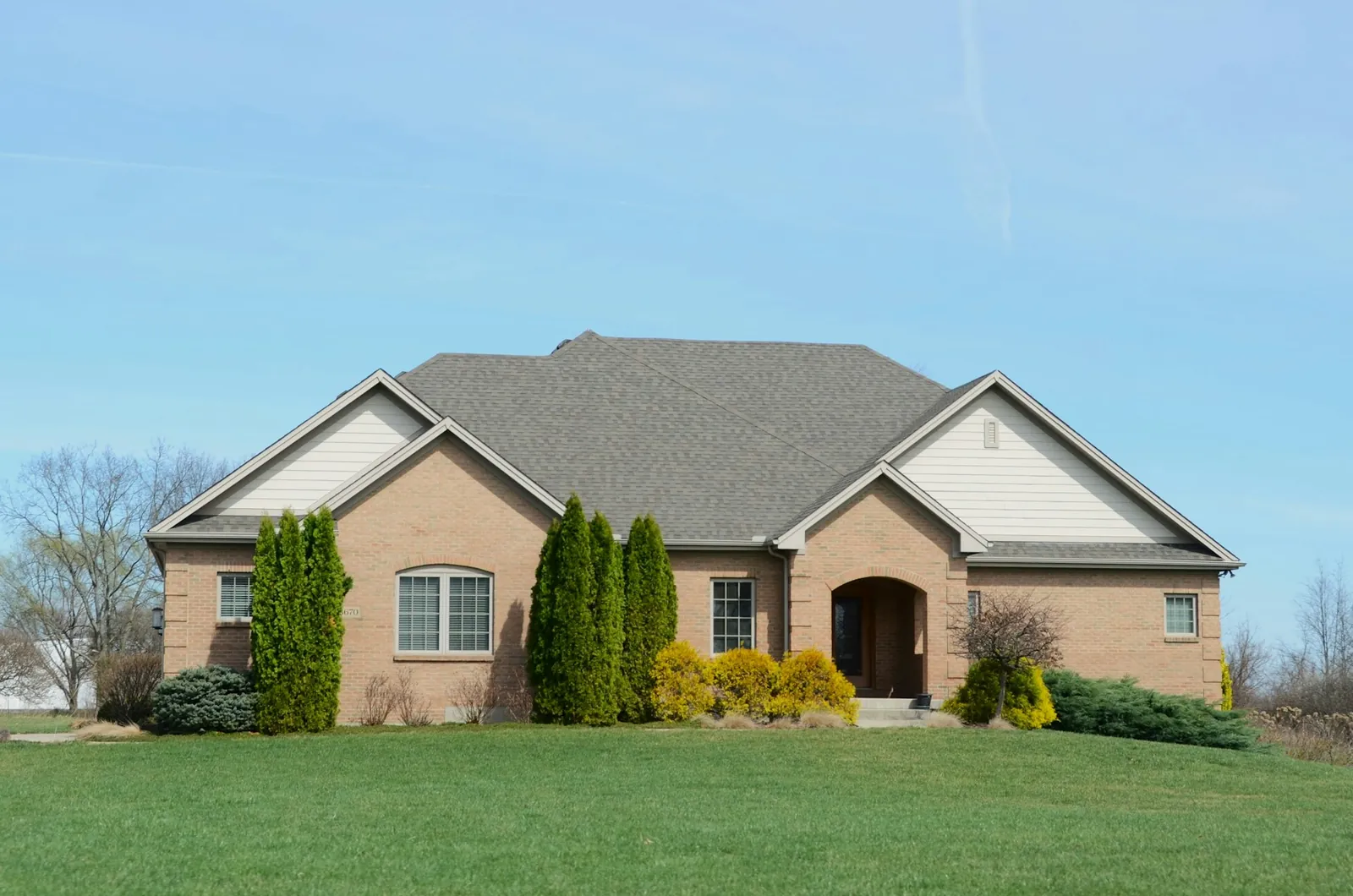 A single-storey brick house with clipped evergreens set back behind a wide, freshly cut front lawn.