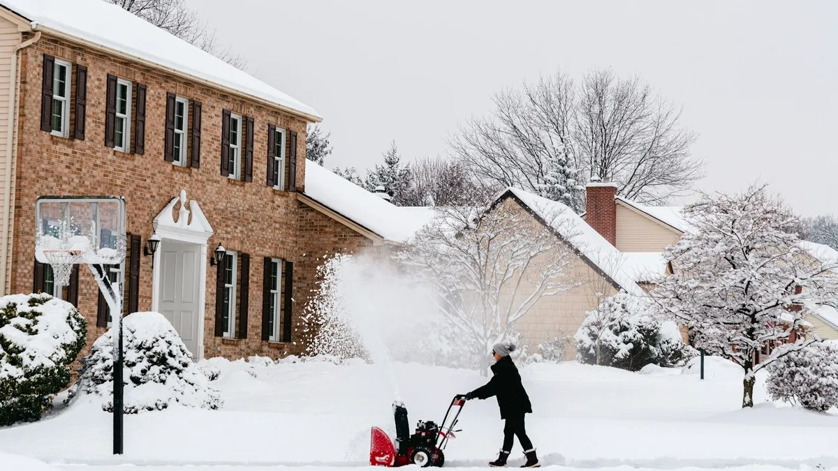 A residential driveway being cleared of deep snow in front of a brick house after a storm.