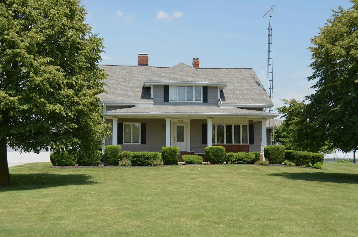A grey farmhouse with clipped foundation shrubs behind a broad, freshly mown front lawn in summer.
