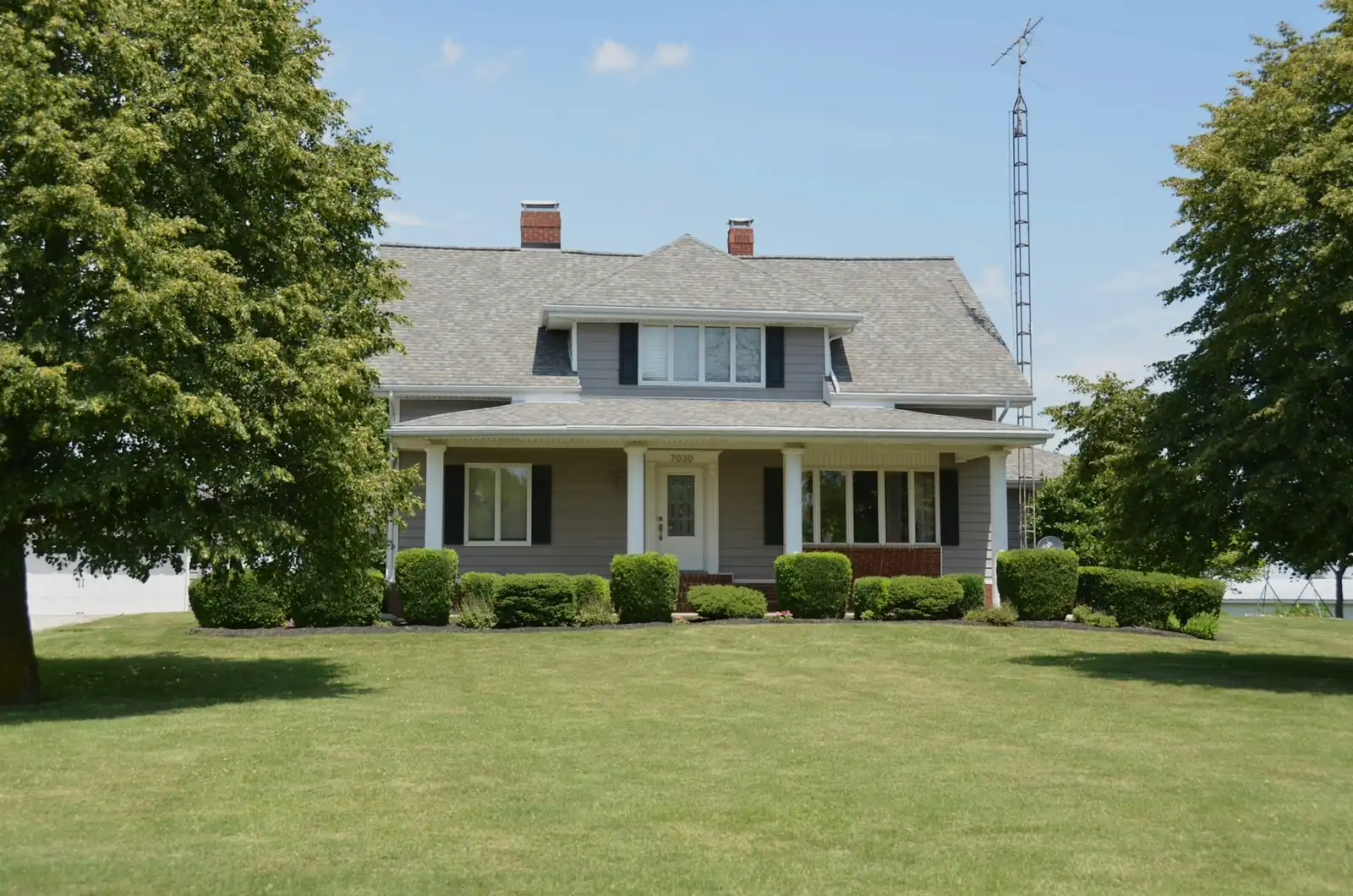 A grey farmhouse with clipped foundation shrubs behind a broad, freshly mown front lawn in summer.