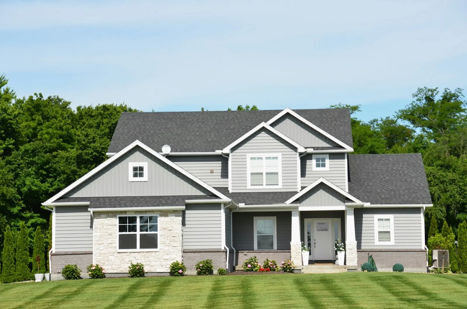 A suburban house behind a wide front lawn cut in fresh mowing stripes on a clear summer day.