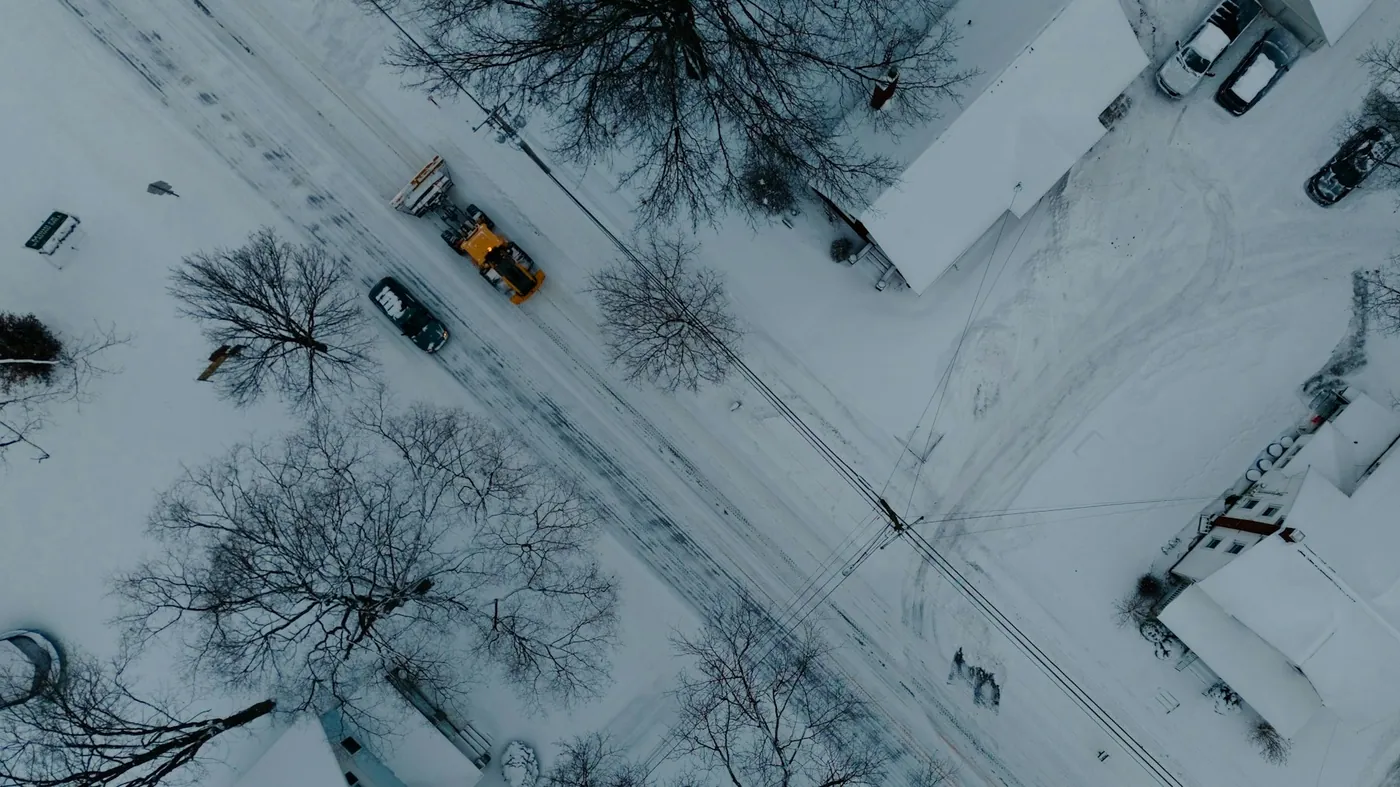 An overhead view of a plow working a snow-covered residential street on a grey winter day.