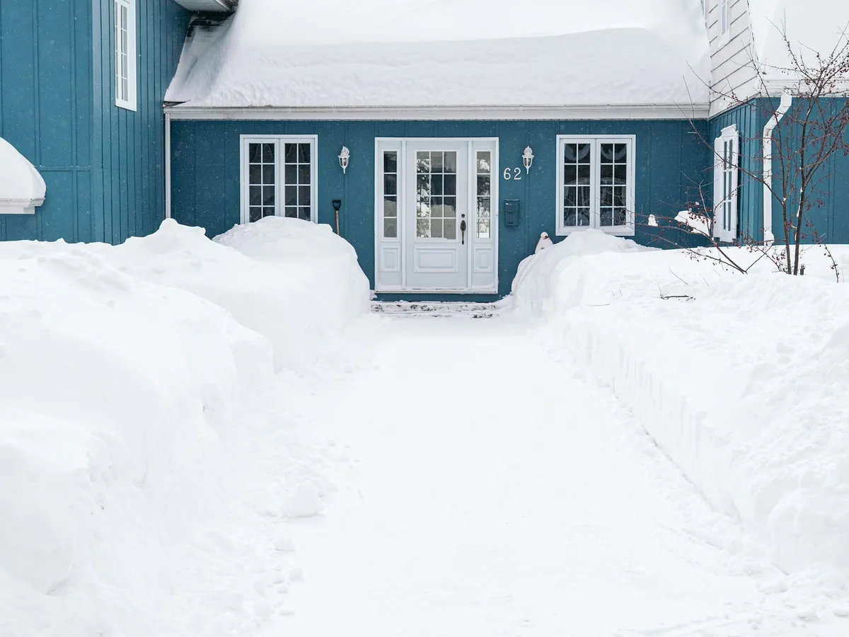 A path shovelled clear from the street to a house's front door, with deep snow banked up on both sides.