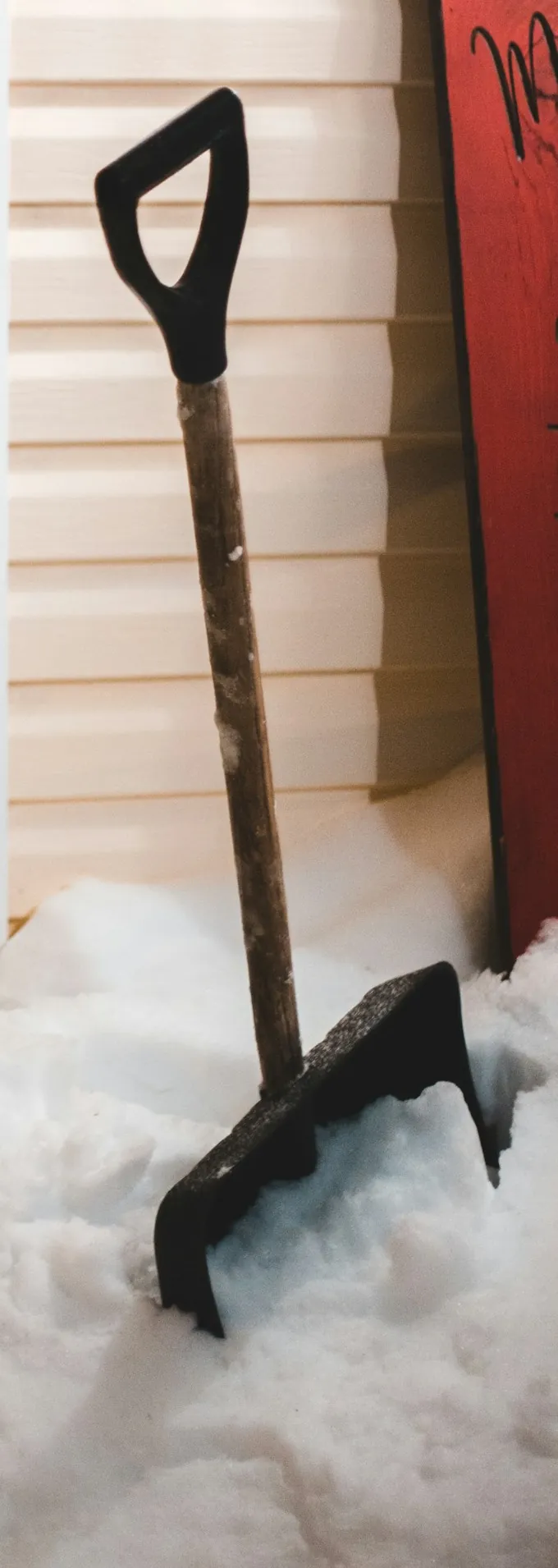 Snow shovels standing in deep snow against the siding of a house after a storm.