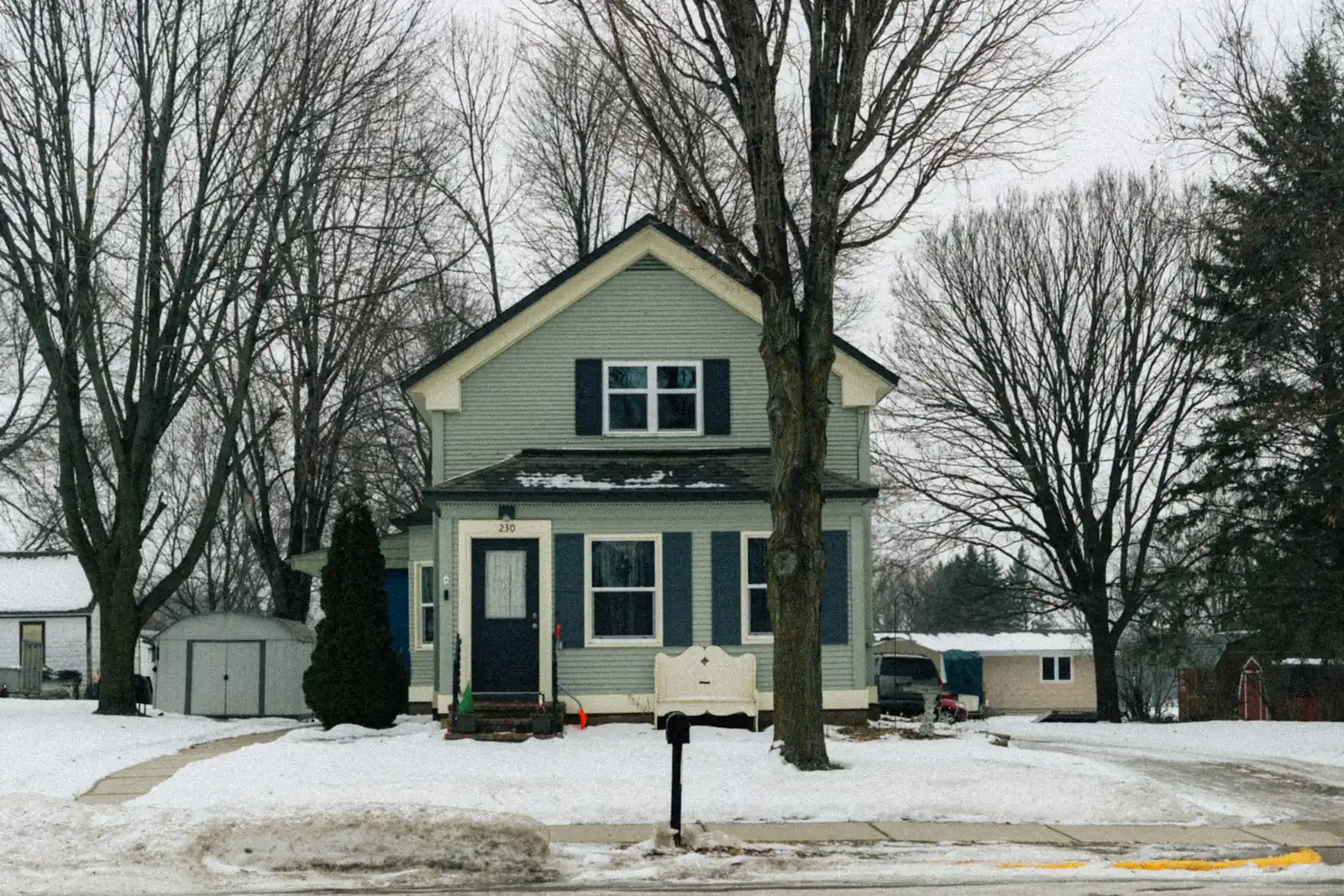 A small-town house on a snow-covered lot with the front walk and the street cleared after a storm.
